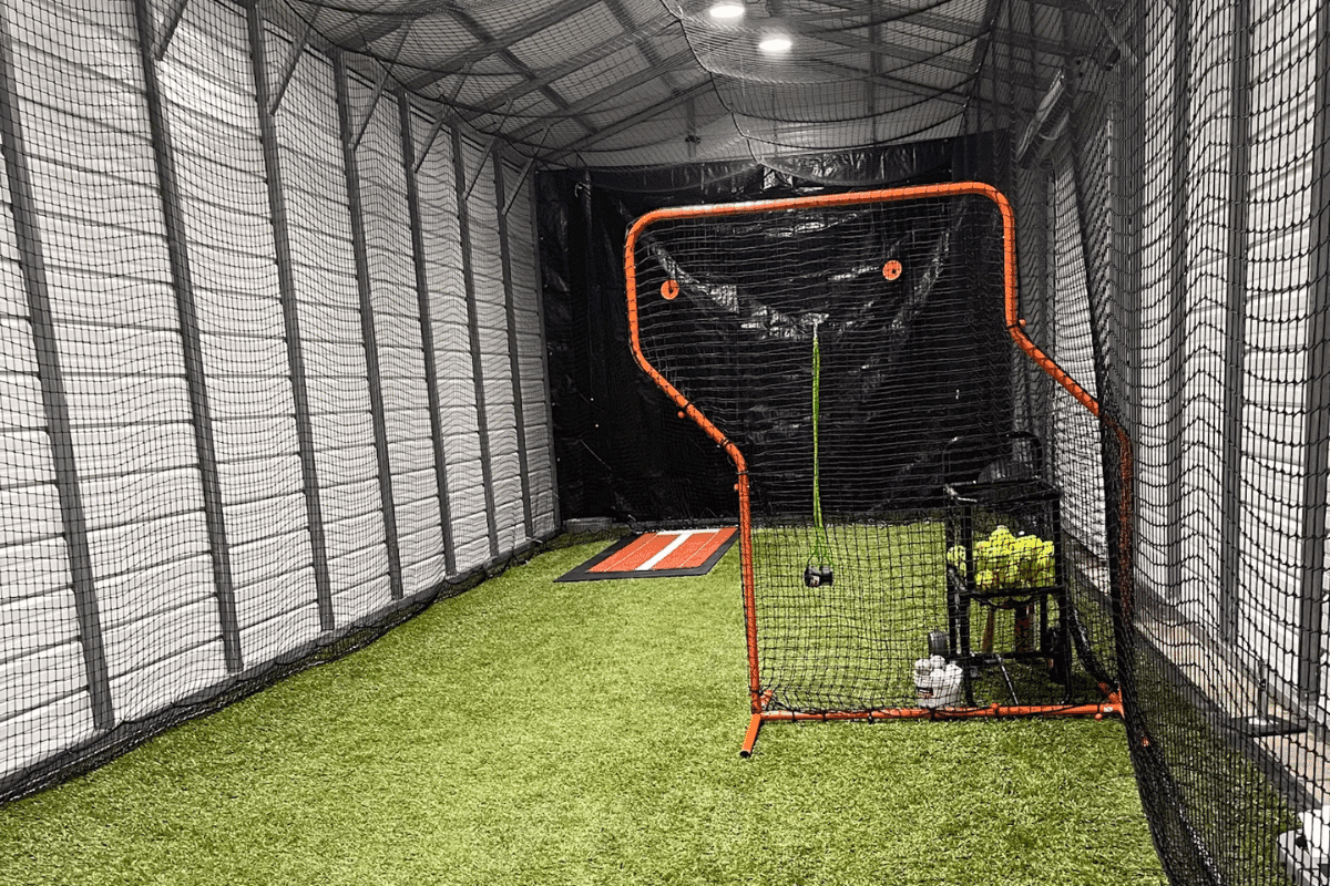A bucket of balls beside a pitching screen in an indoor batting cage
