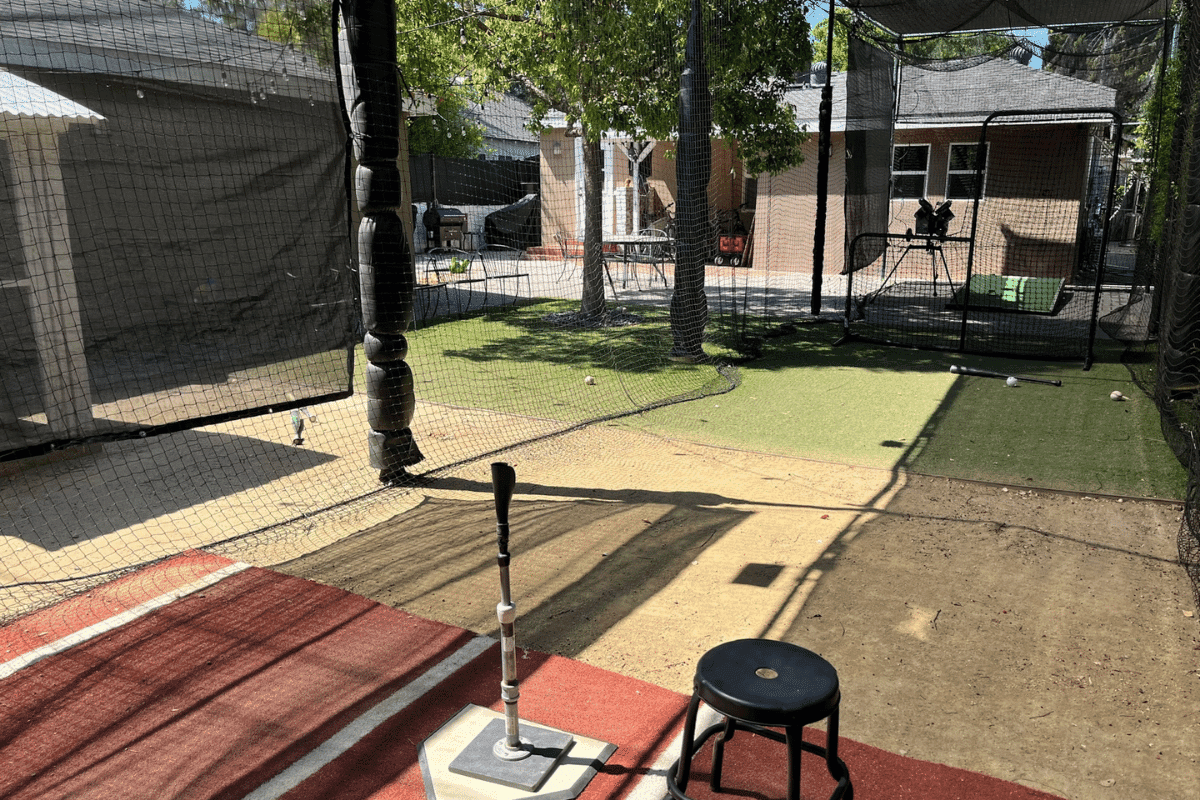 A batting tee and bat set up at the plate in a backyard cage