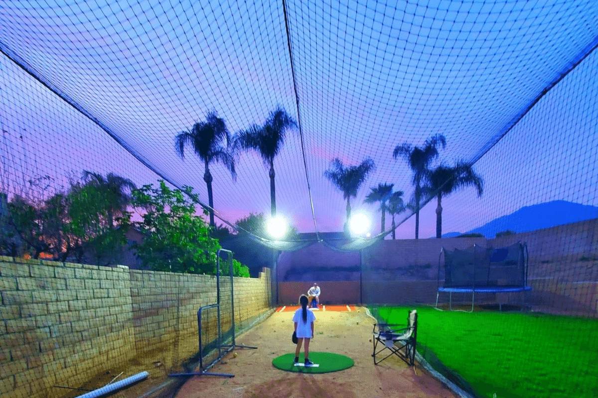 Premium backyard batting cage with LED lighting at sunset