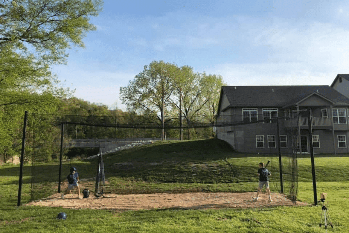 Two players taking batting practice together in a backyard cage