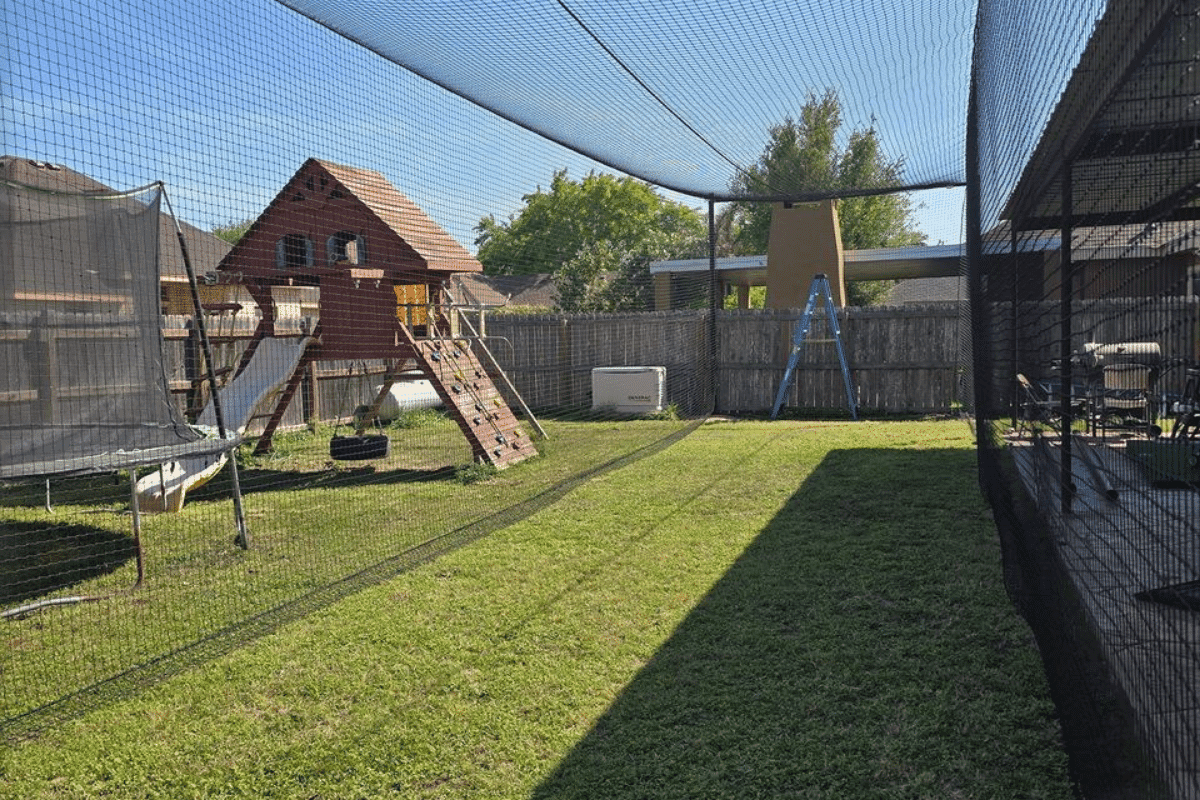 Family backyard batting cage next to a playground and trampoline