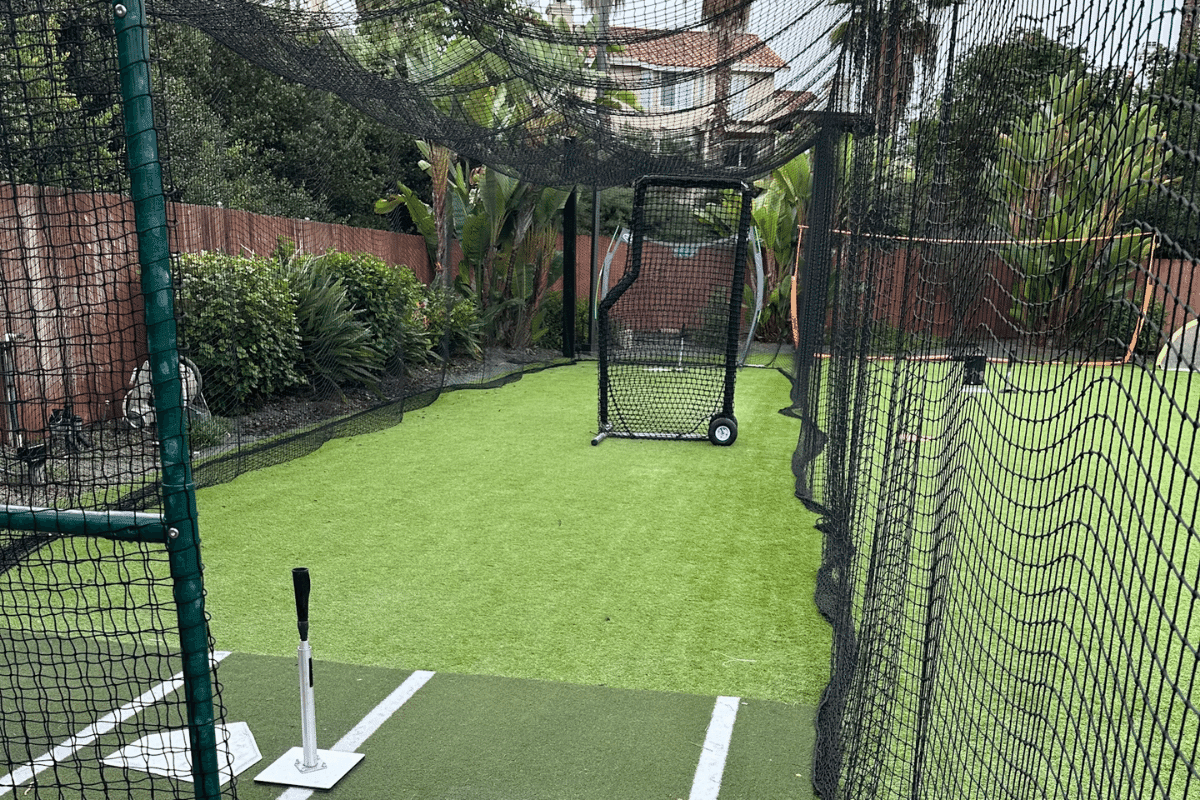 A pitching machine set down-cage in a turfed backyard batting cage