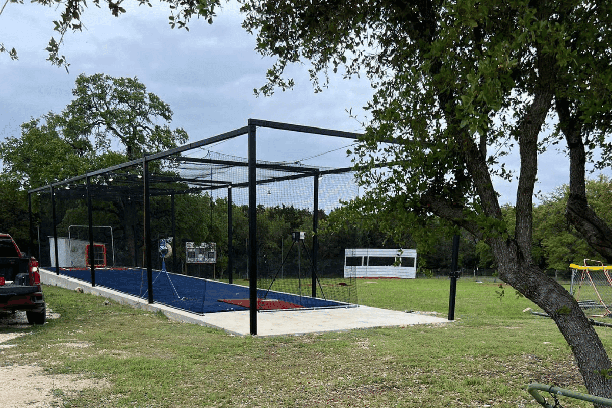 A completed backyard batting cage on a concrete pad with netting and turf