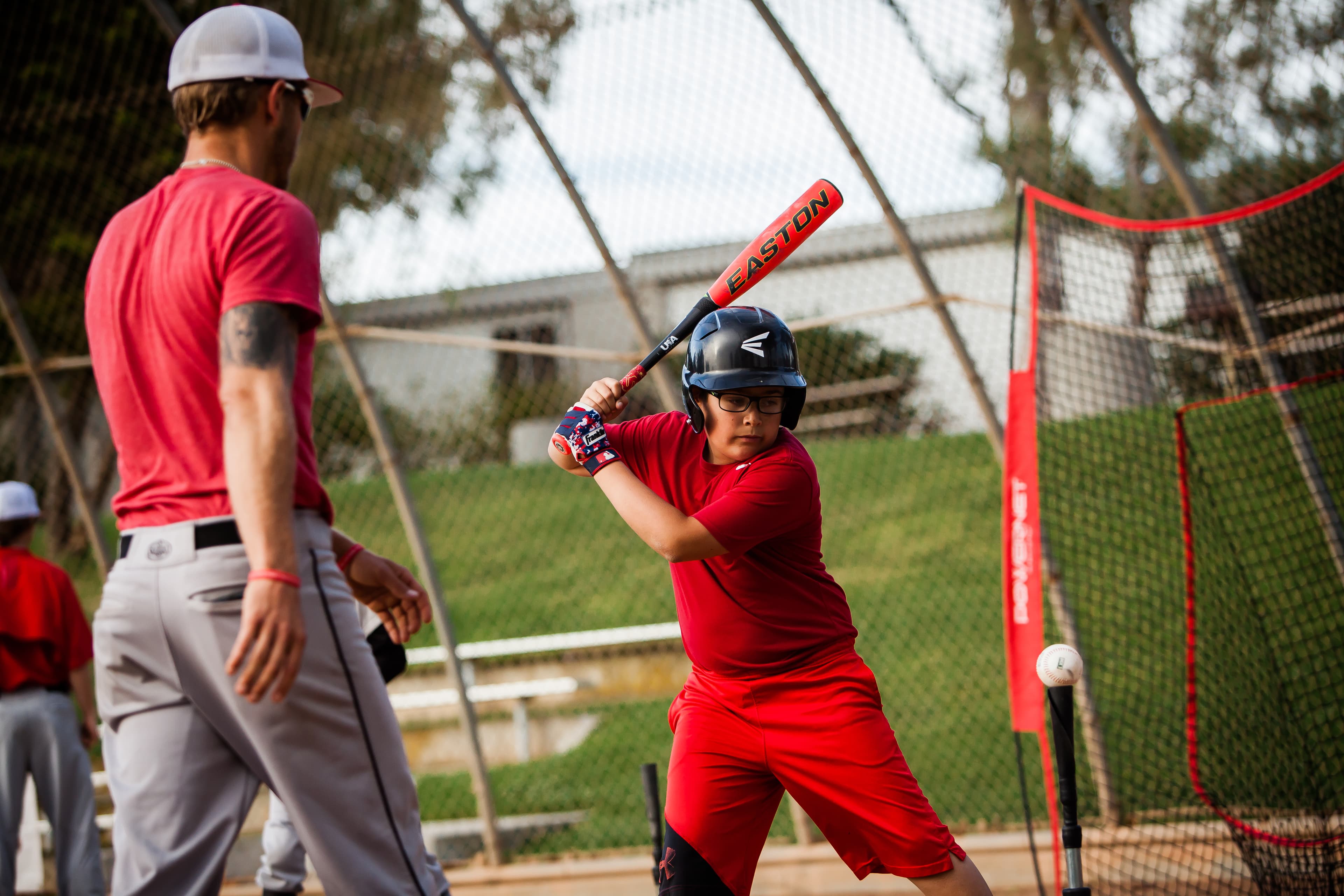 A coach watching a young hitter take swings in a cage