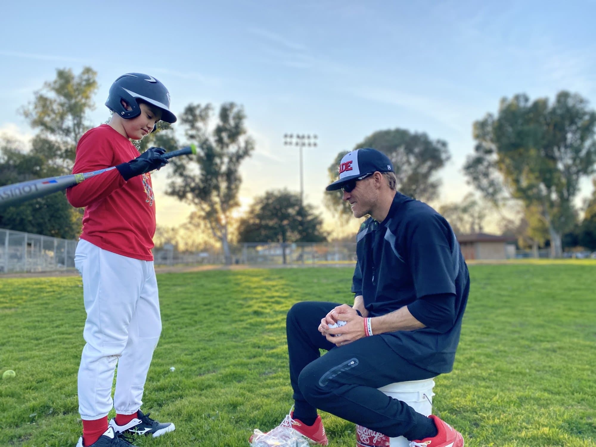Isaac Hess coaching a young hitter at a Los Angeles park at sunset