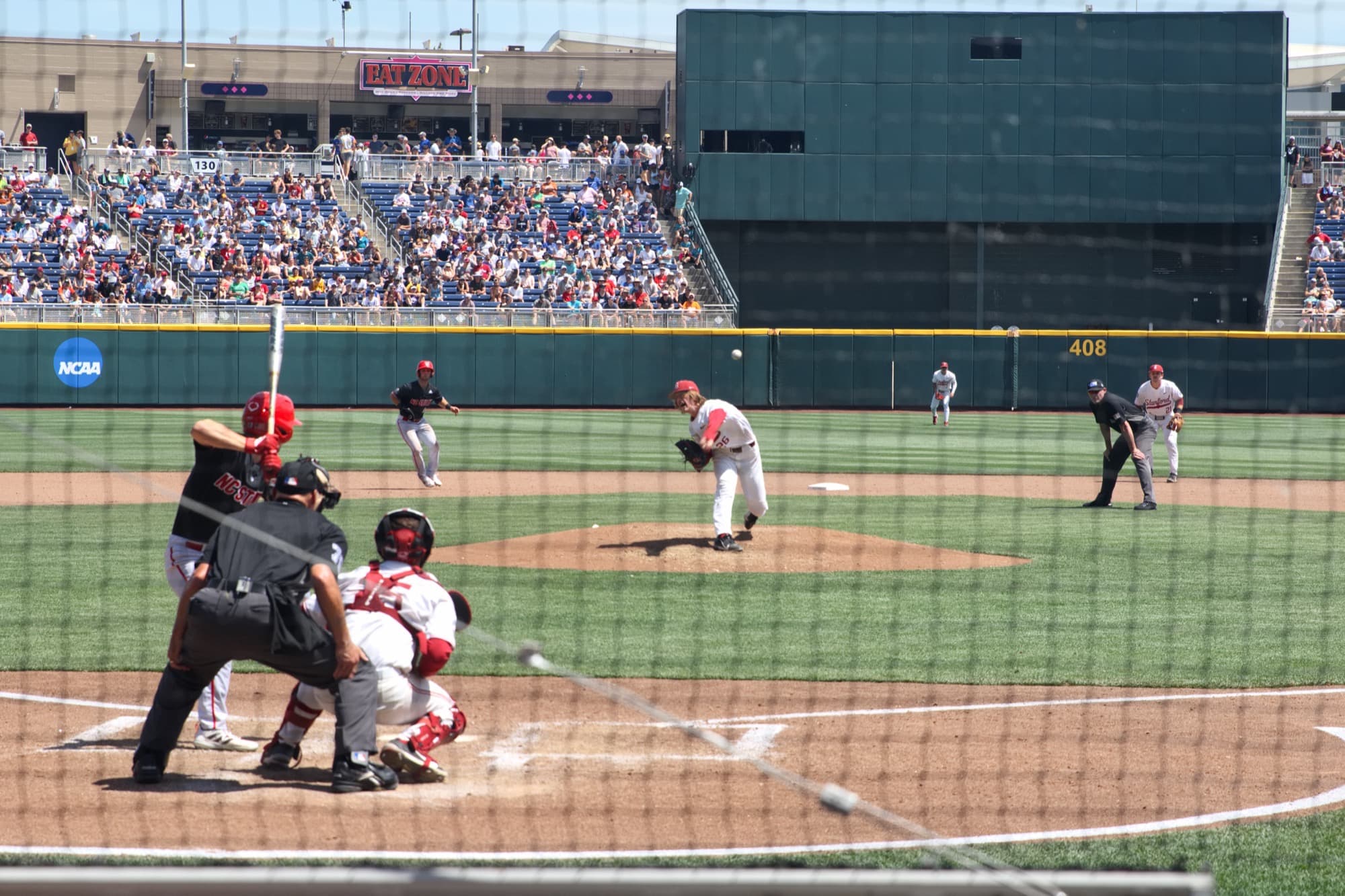 A pitcher delivers during a 2021 College World Series game in Omaha, seen through the backstop netting