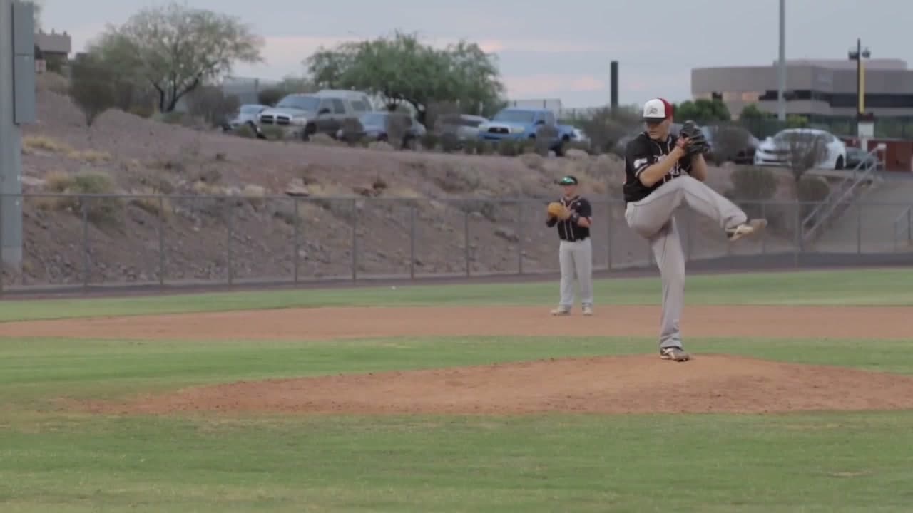 Isaac Hess at the top of his leg lift on the mound in a black jersey and red and white cap during a game in Arizona