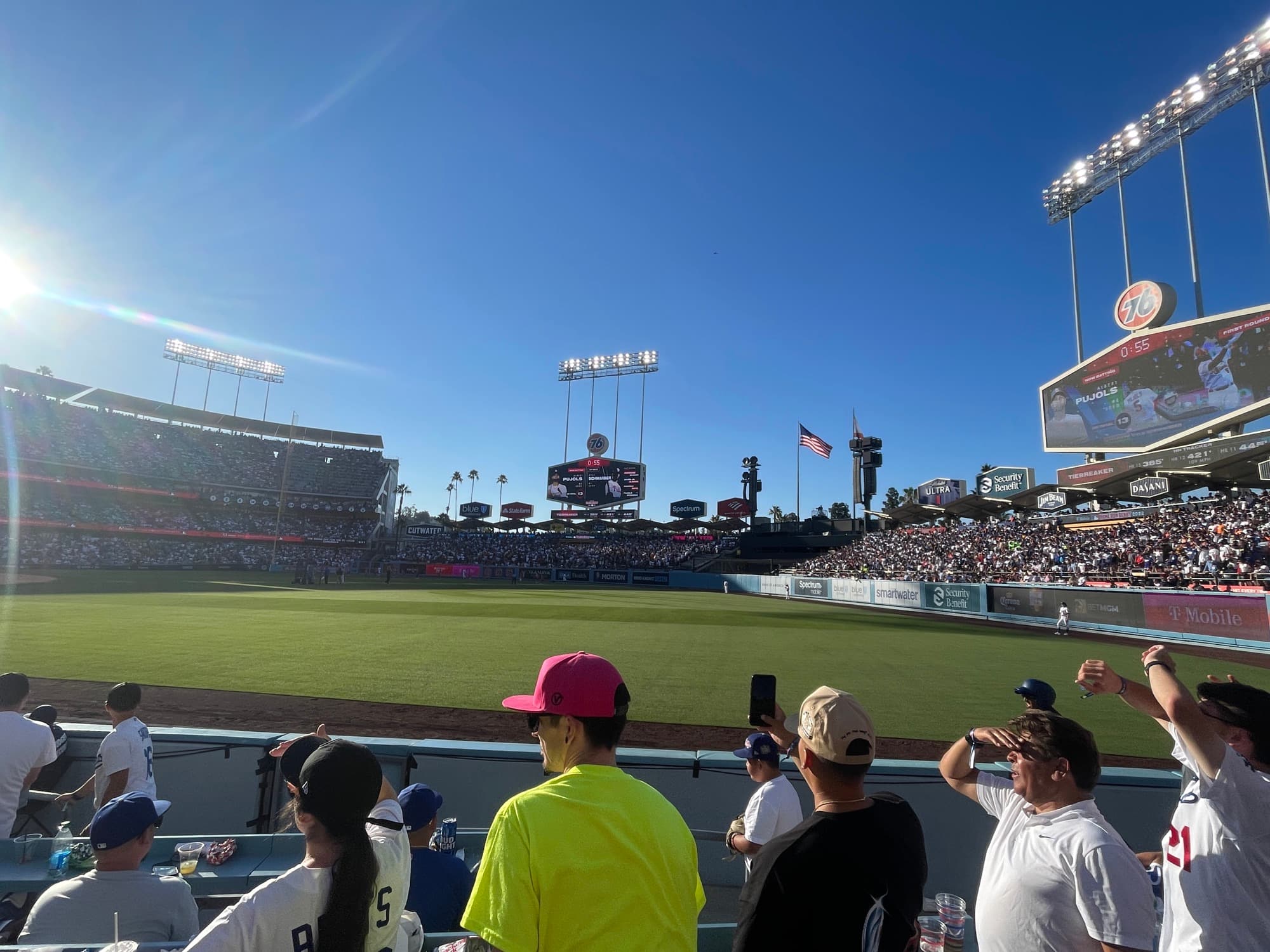 A ballpark outfield and stands on an afternoon, seen from the pavilion under a clear sky