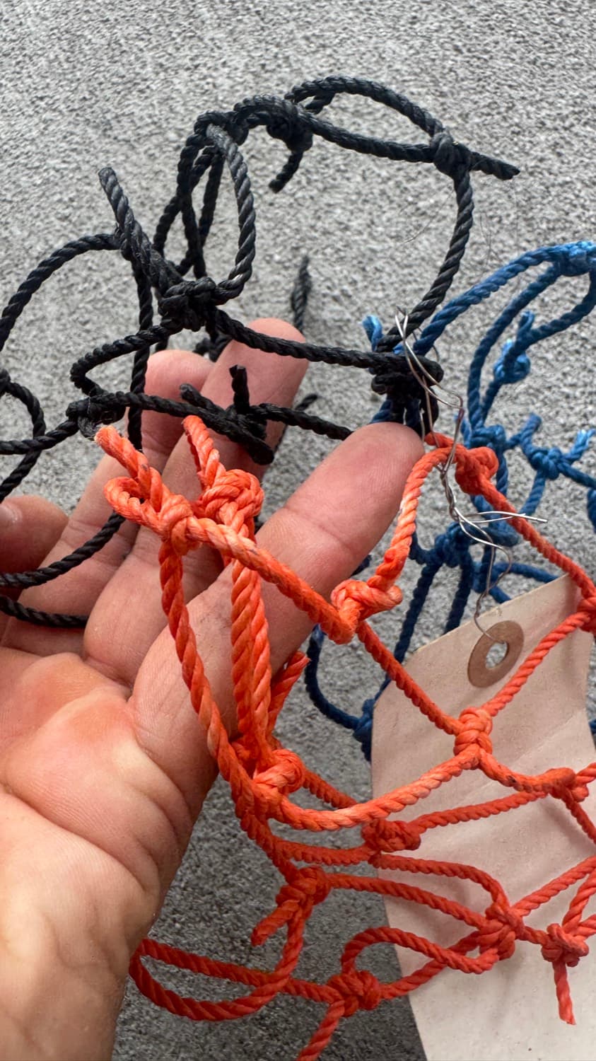 A hand holding sample squares of knotted batting cage netting in black, orange and blue
