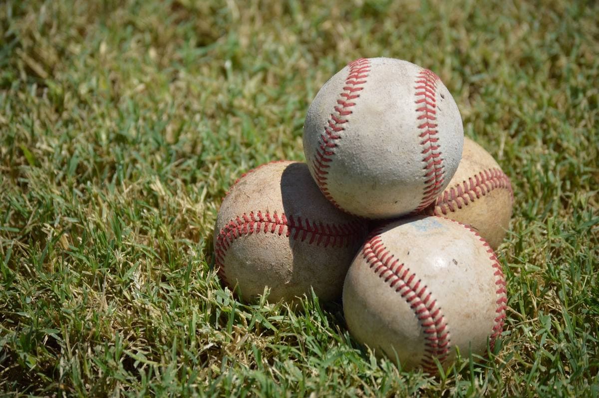 Four scuffed baseballs stacked on outfield grass