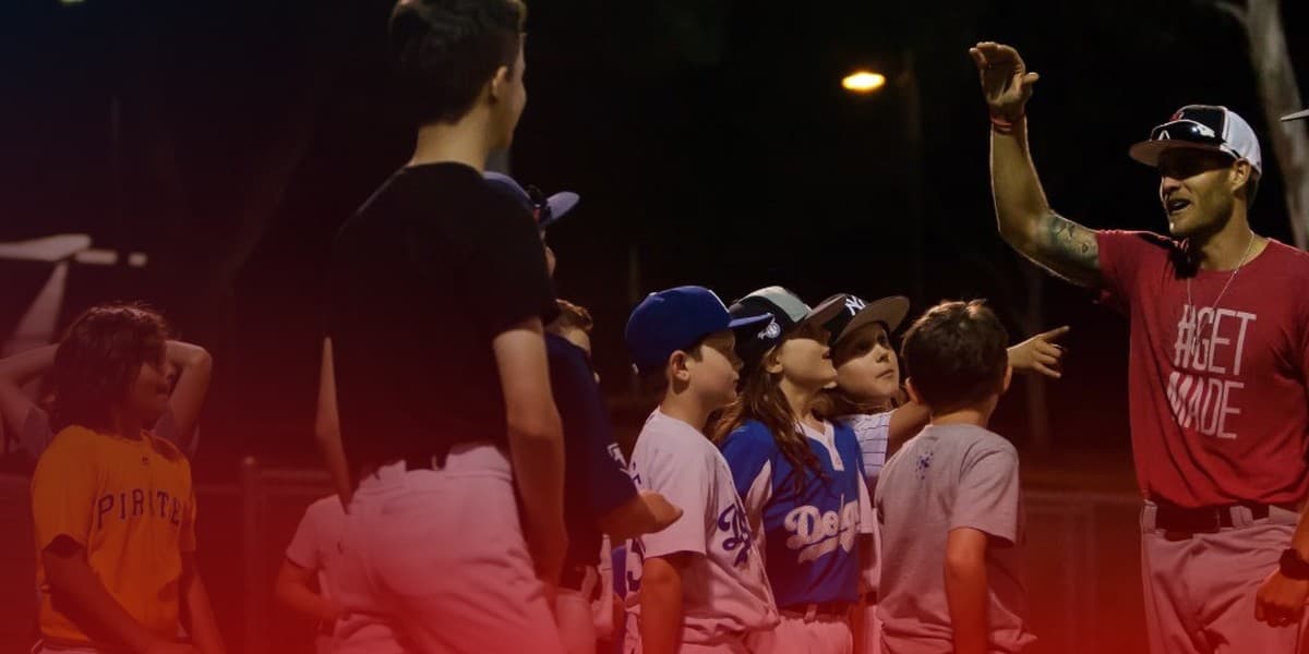 A coach under the lights talking to a group of young players after a session