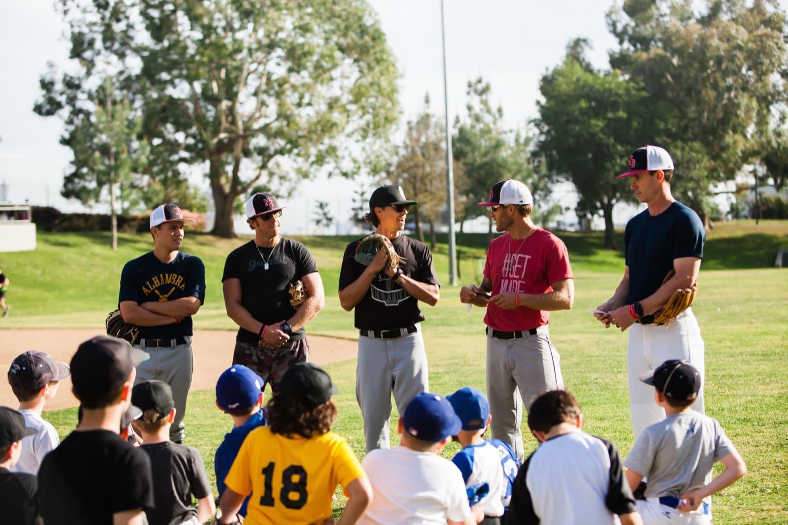 Five coaches standing in front of a seated group of young players at an outdoor practice