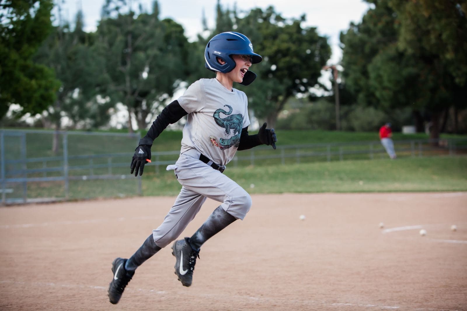 A young base runner in a batting helmet sprinting hard down the baseline