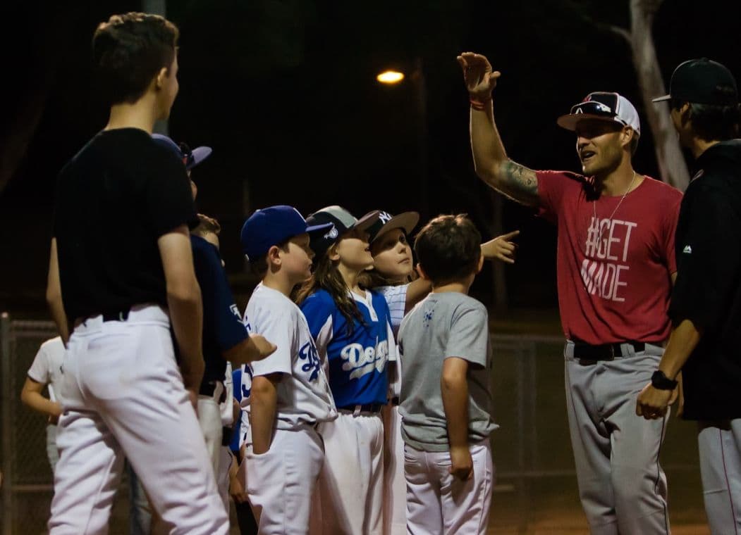 Coach Isaac Hess in a #GETMADE shirt, arm raised, rallying young players under the lights