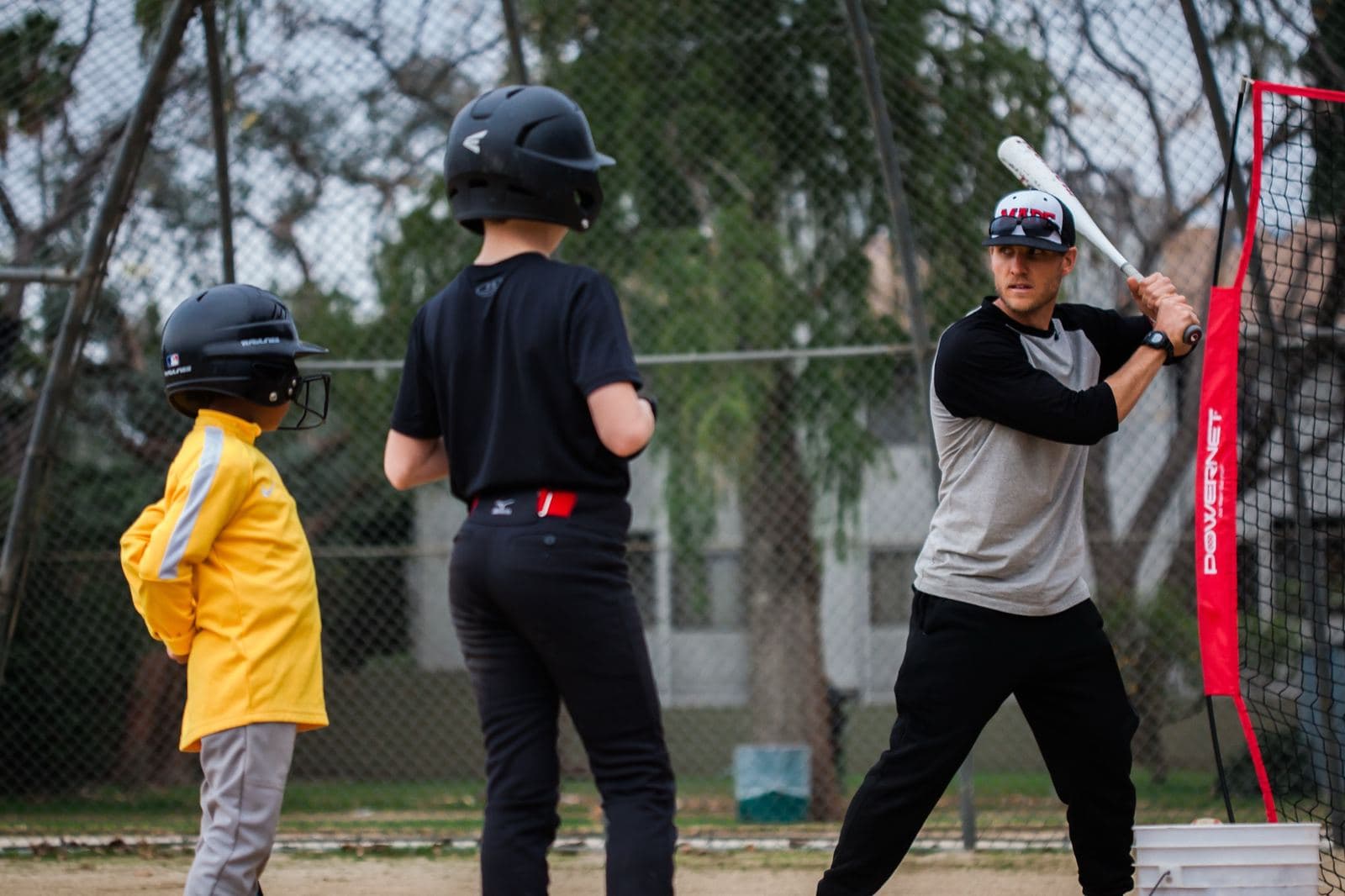 Coach Isaac Hess demonstrating a batting stance while two young players watch