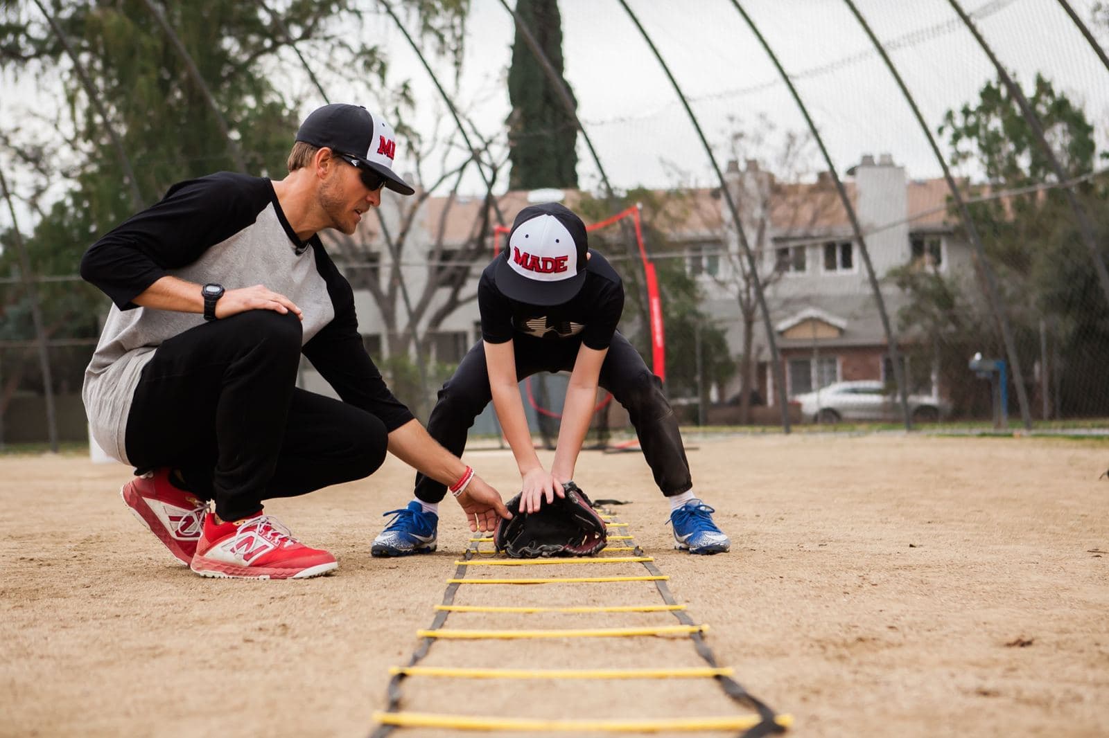 Coach Isaac Hess crouching beside a young player to set his glove hands on the ground at a fielding drill