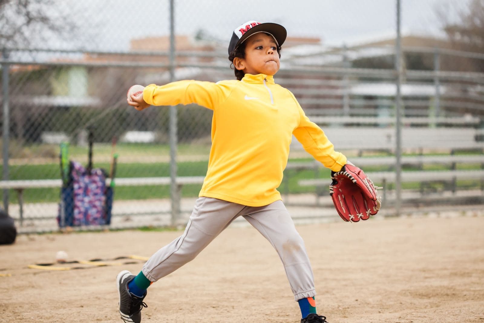 A young pitcher in a yellow pullover mid-throw with his glove out front