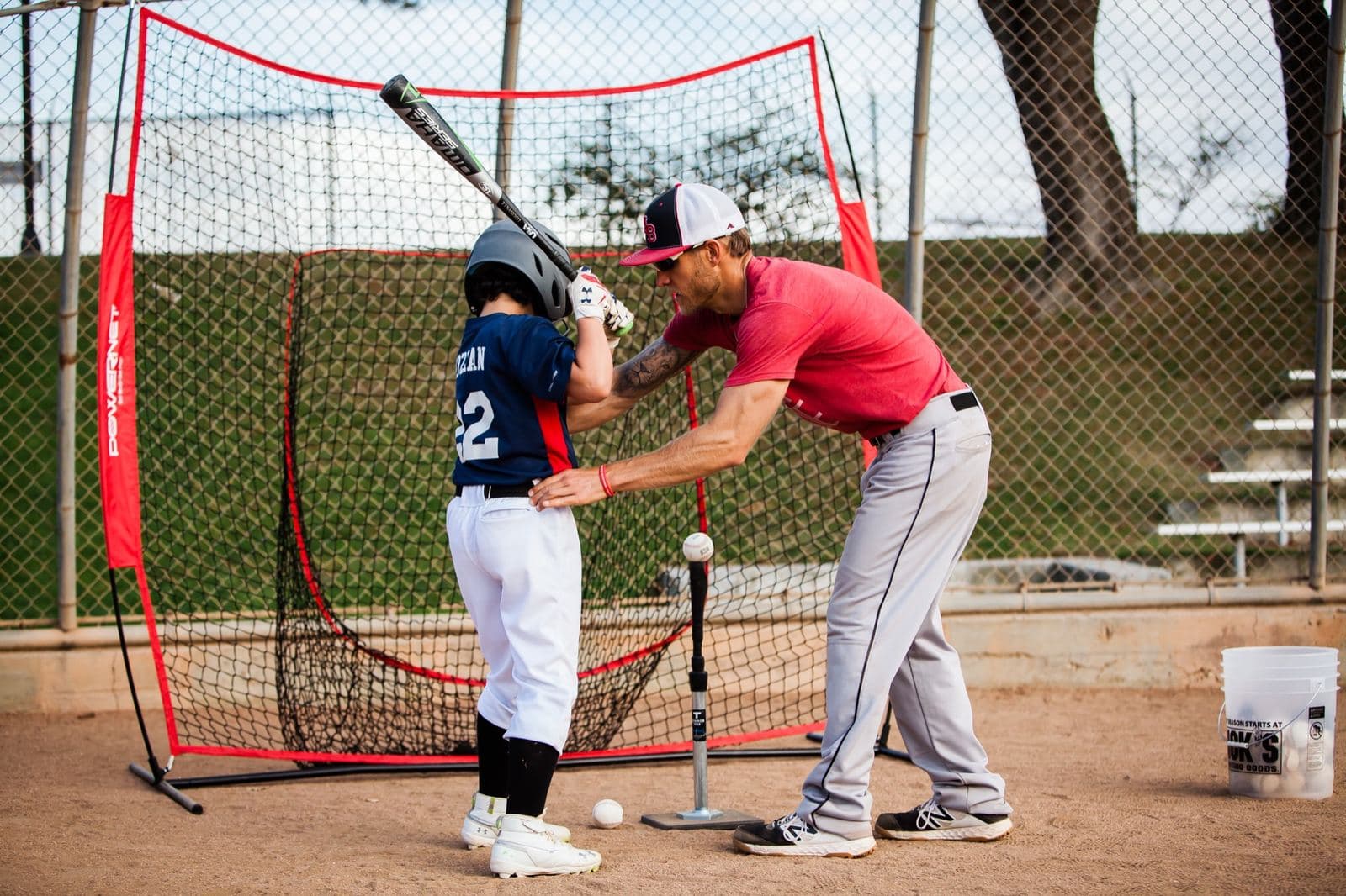 A coach setting a young beginner's hands on the bat at a batting tee