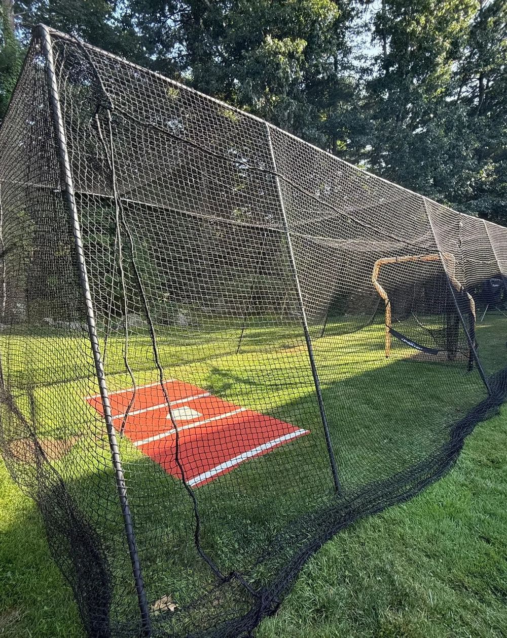 A backyard batting cage with a hitting mat on the lawn