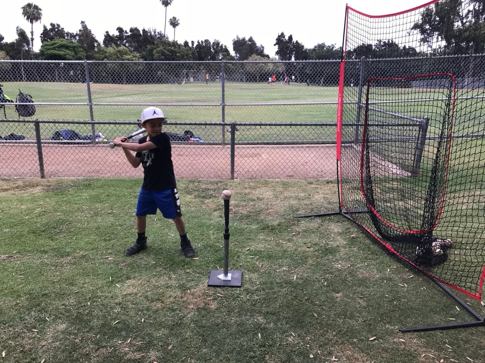A young player hitting off a tee into a portable net on a grass field