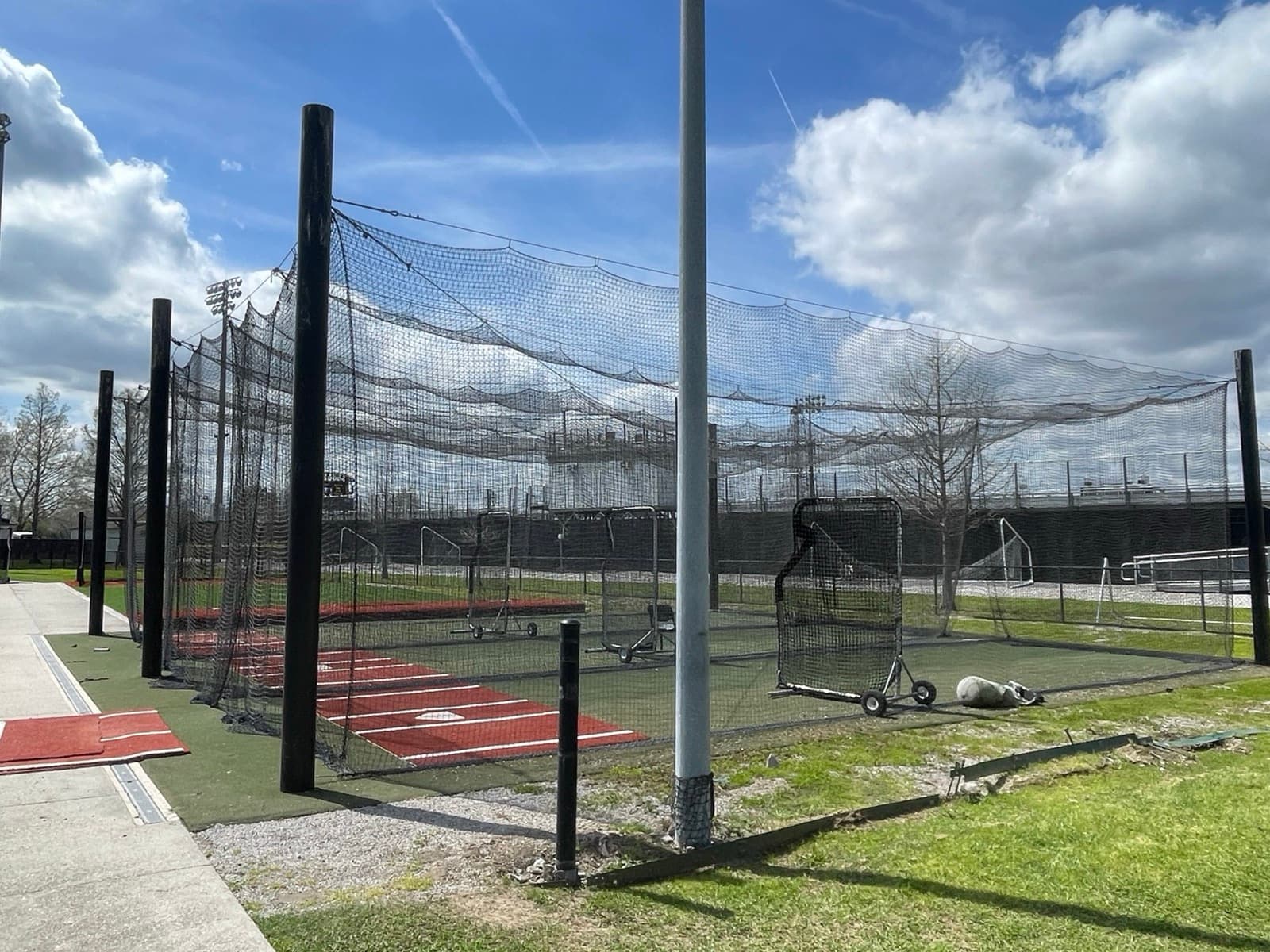 Outdoor batting cage tunnels with nets and L-screens beside a ball field