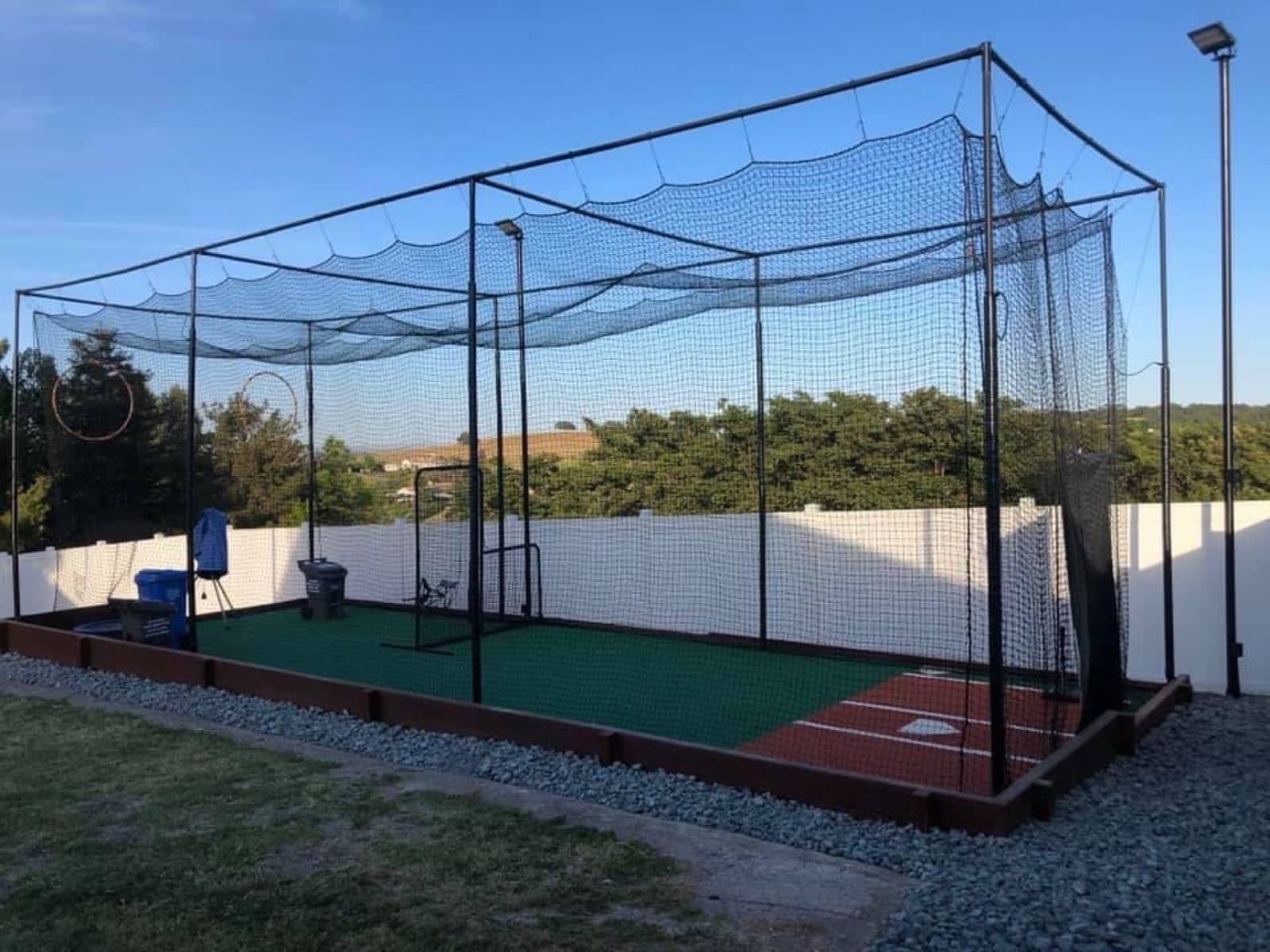 A backyard batting cage with netting, a steel frame, turf, lights, an L-screen and a pitching machine