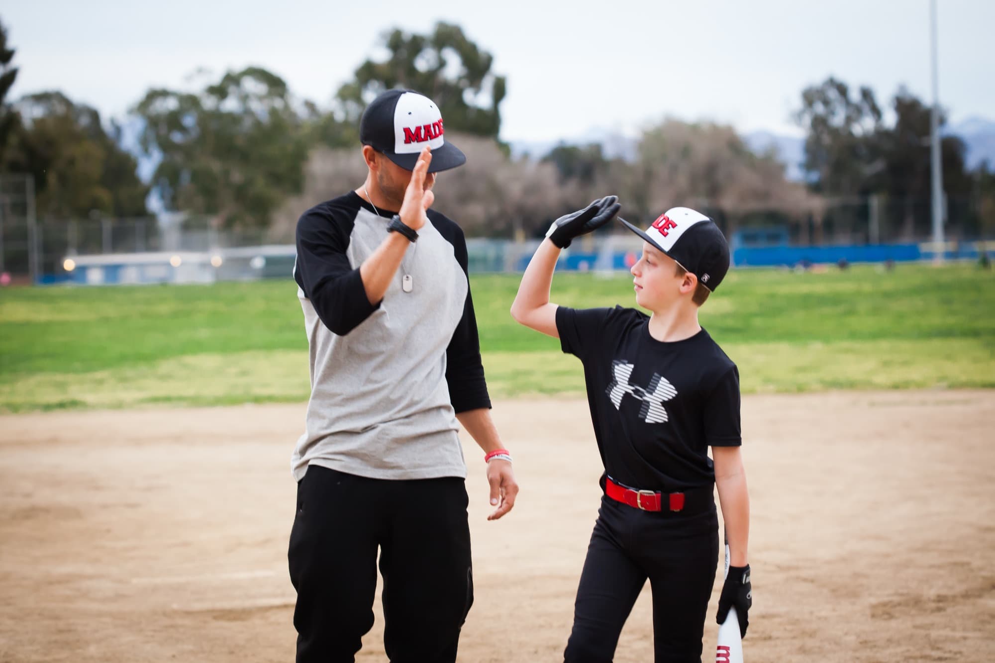 A coach high-fives a young player on the infield