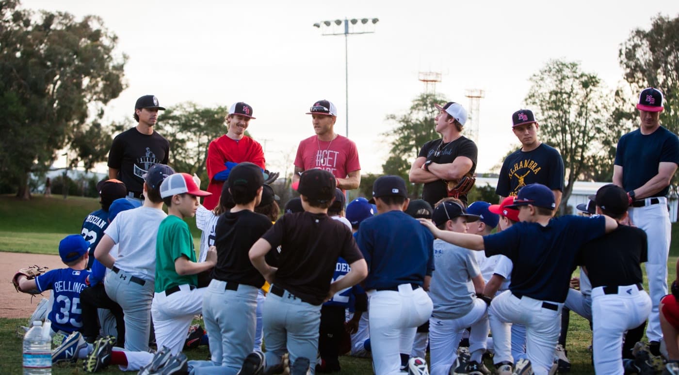 Coaches talking to a group of young players kneeling on the grass at a MADE Baseball camp