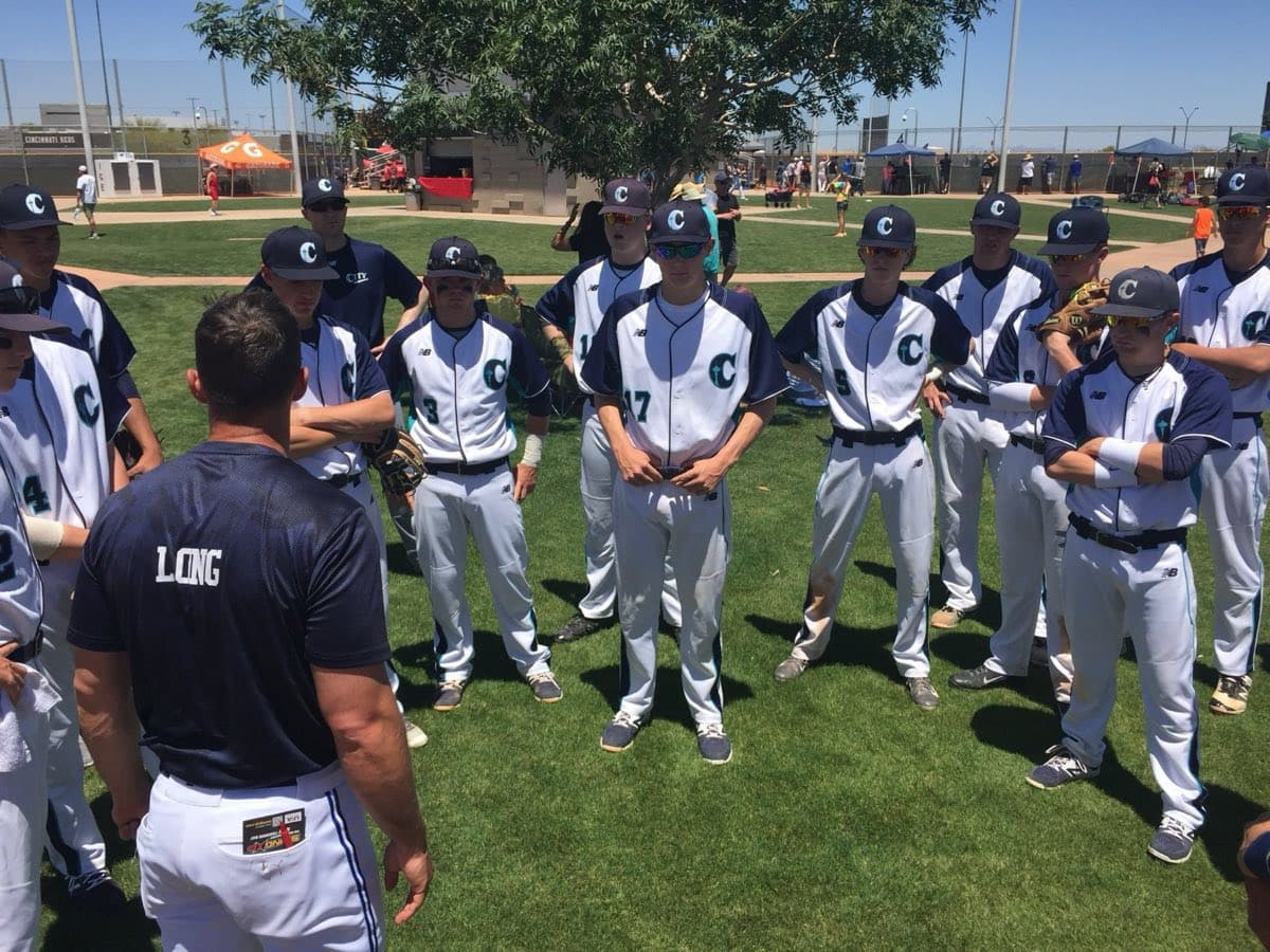 A travel team huddled around their coach on the outfield grass