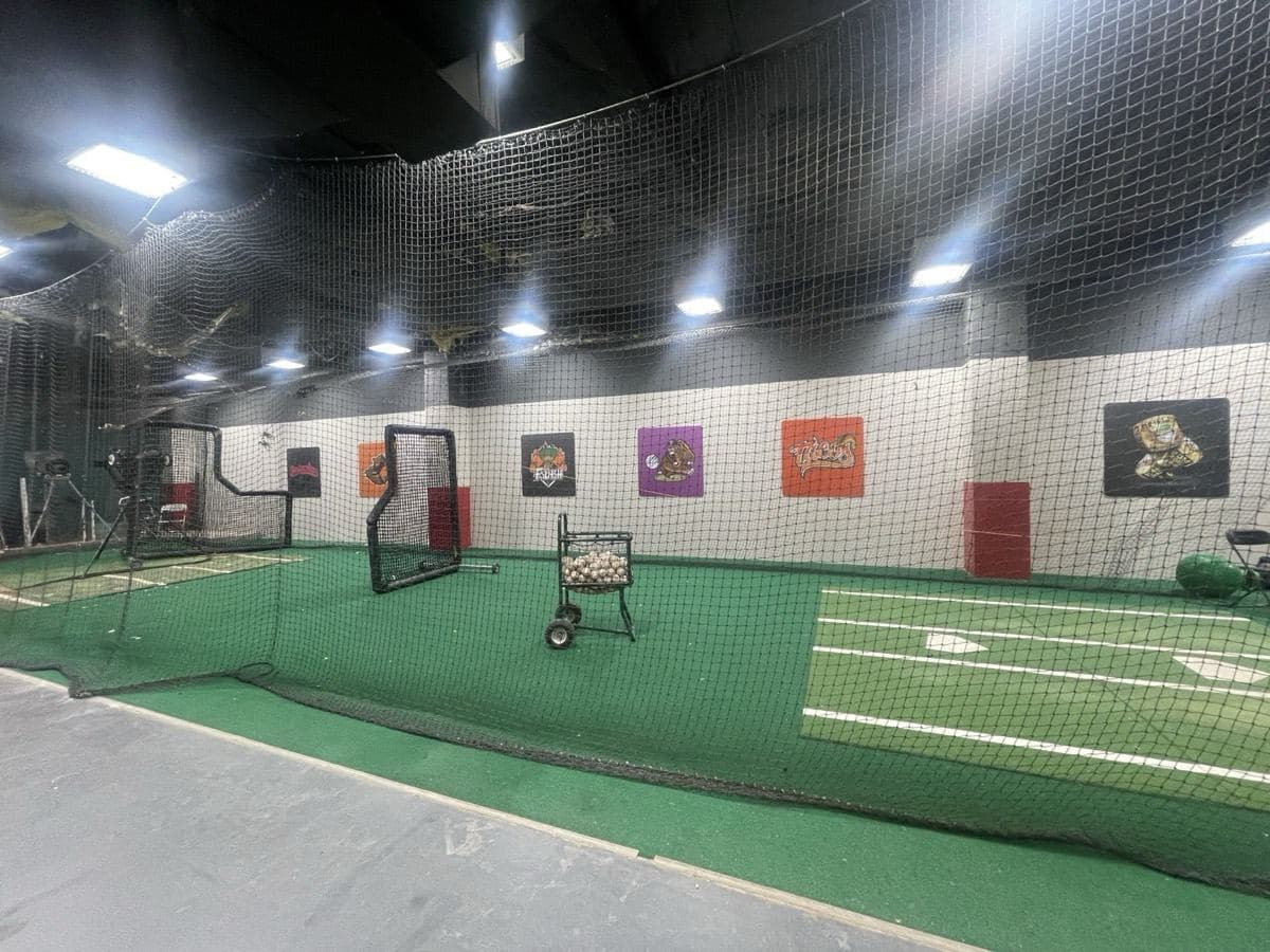 An empty indoor batting cage with turf and a pitching screen