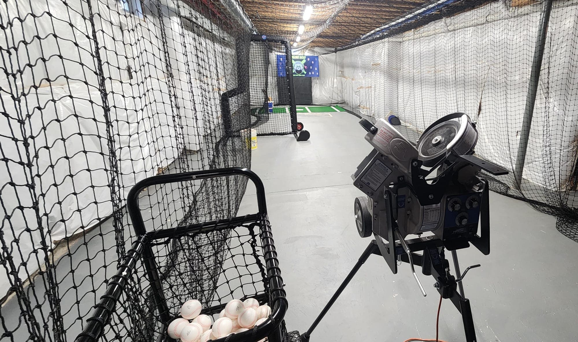 Long indoor netted tunnel with concrete floor, ball cart and pitching machine