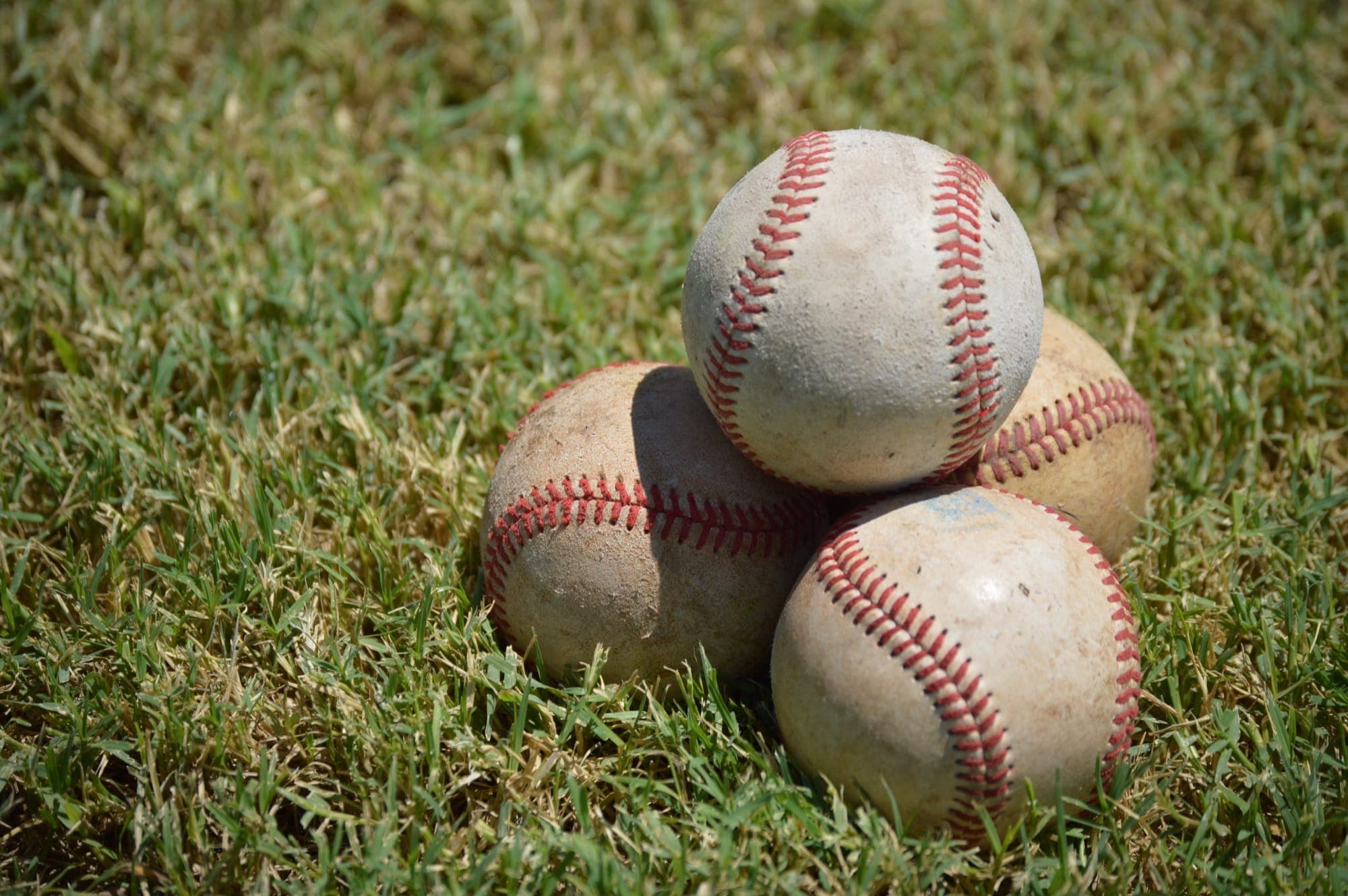 Four scuffed baseballs sitting in the grass