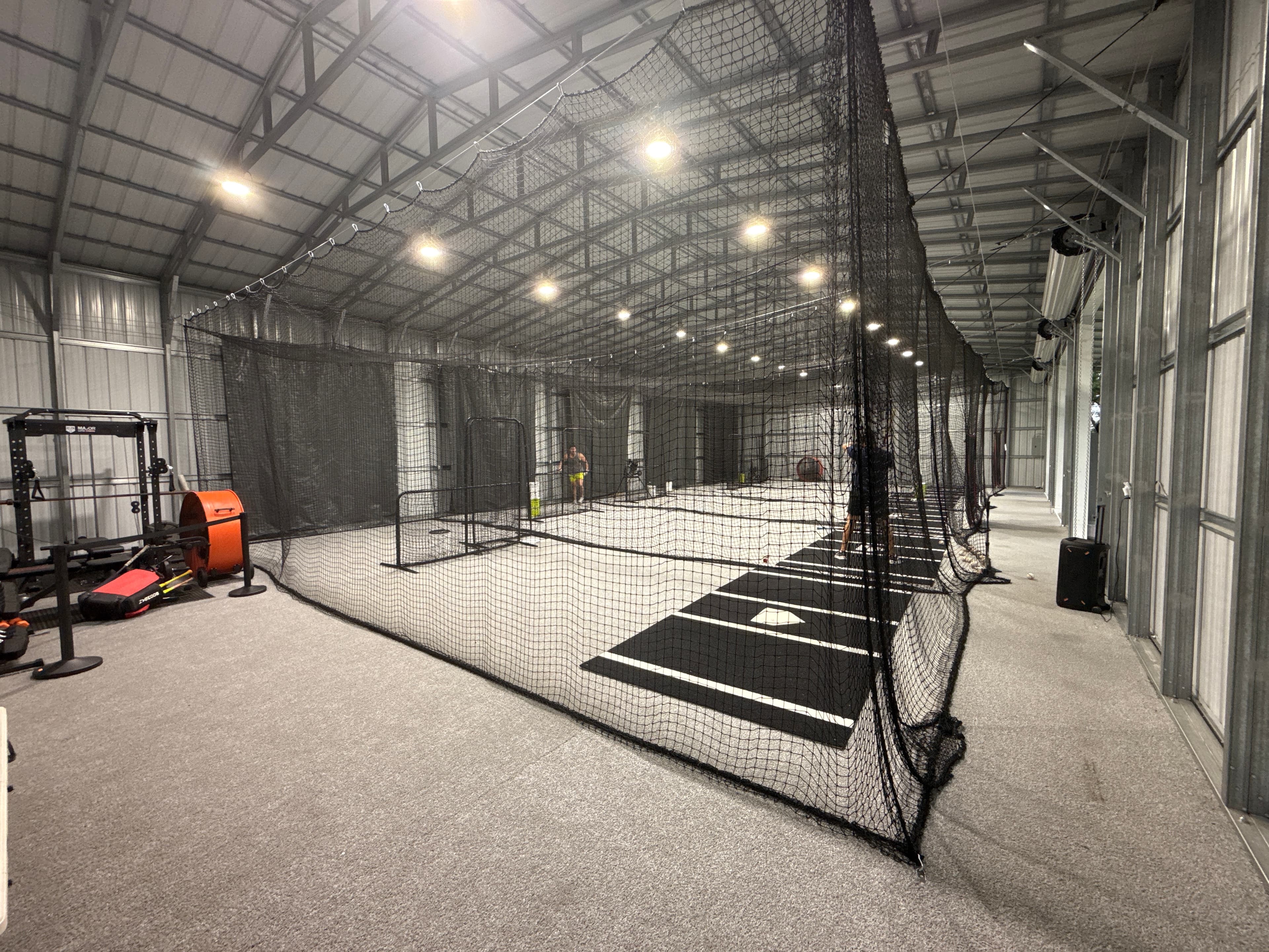 The indoor floor at Swing Kingz in St Cloud, Florida: turf hitting lanes and netting under an open warehouse ceiling