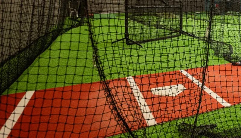 Home plate and green turf seen through the cage netting at Wrecking Yard Baseball
