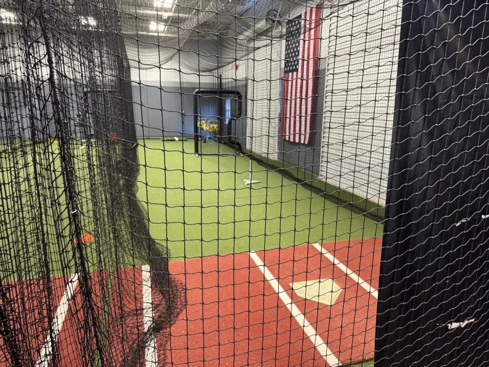 An indoor hitting lane at MPH Warehouse in Orlando, with red clay-coloured turf, a home plate and netting