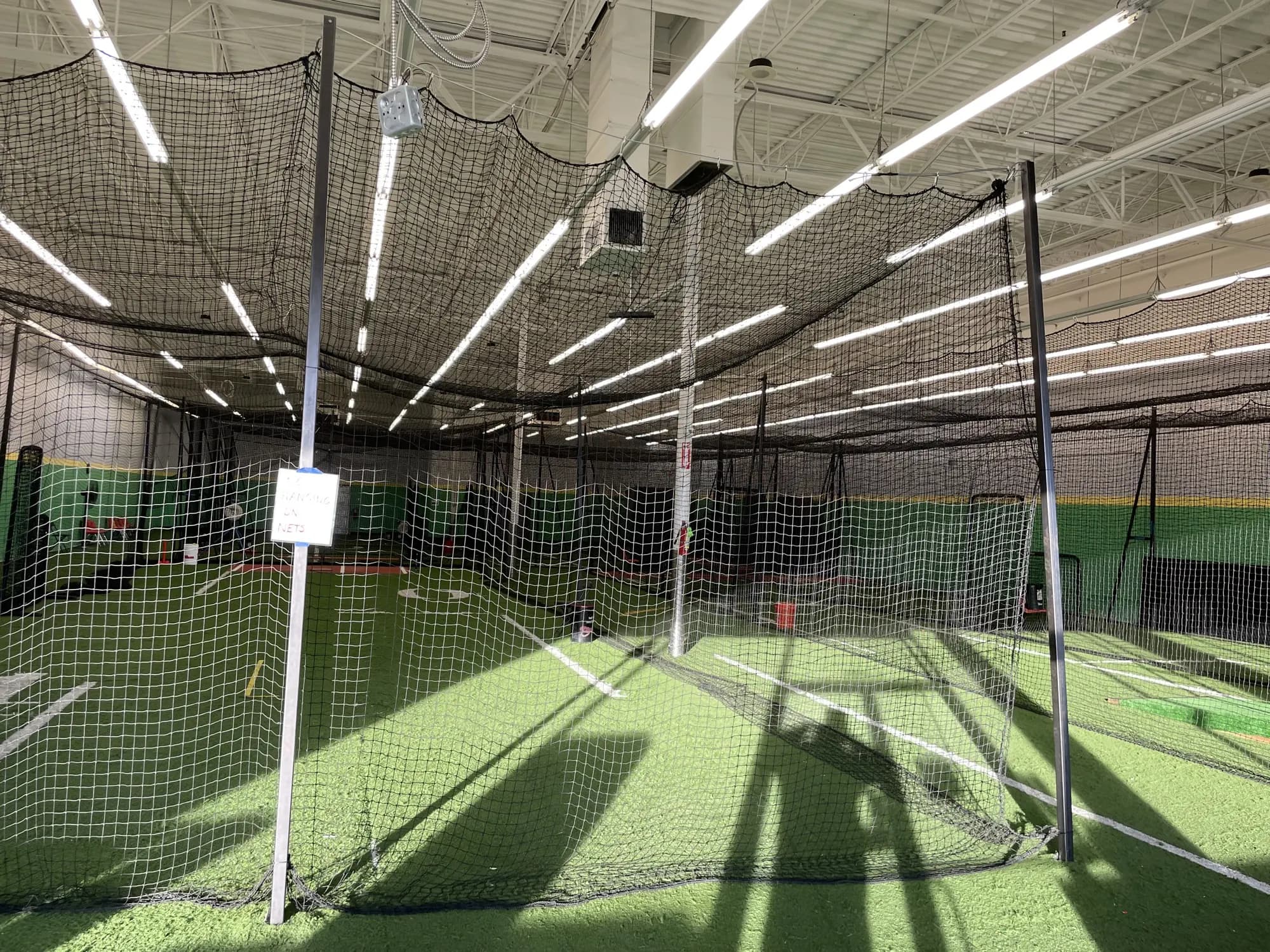 Empty batting cages at Top Prospects, seen from inside the retractable netting looking across the turf toward the padded green back wall
