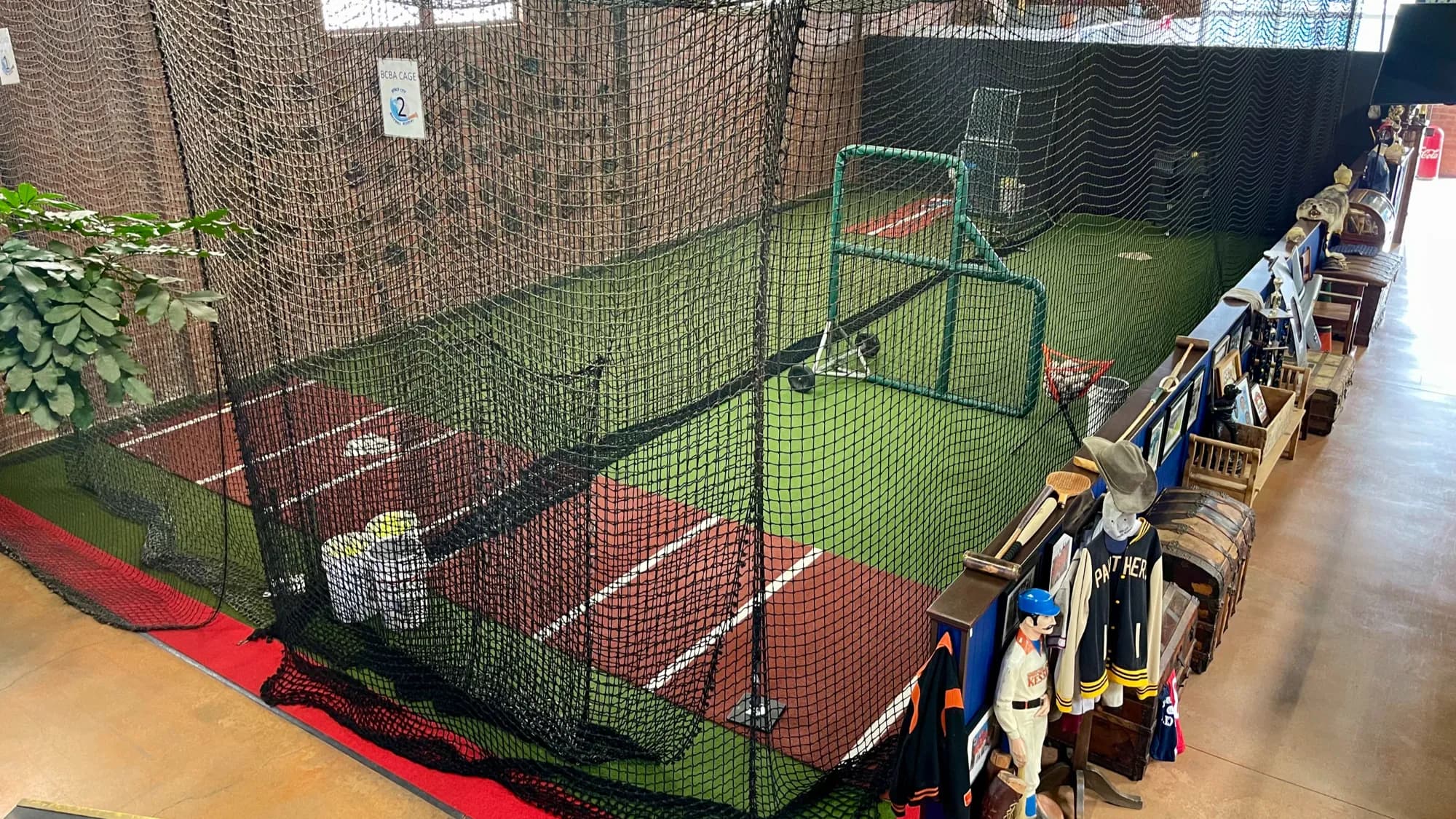 A turf batting cage lane with a pitching machine at Beach City Baseball Academy