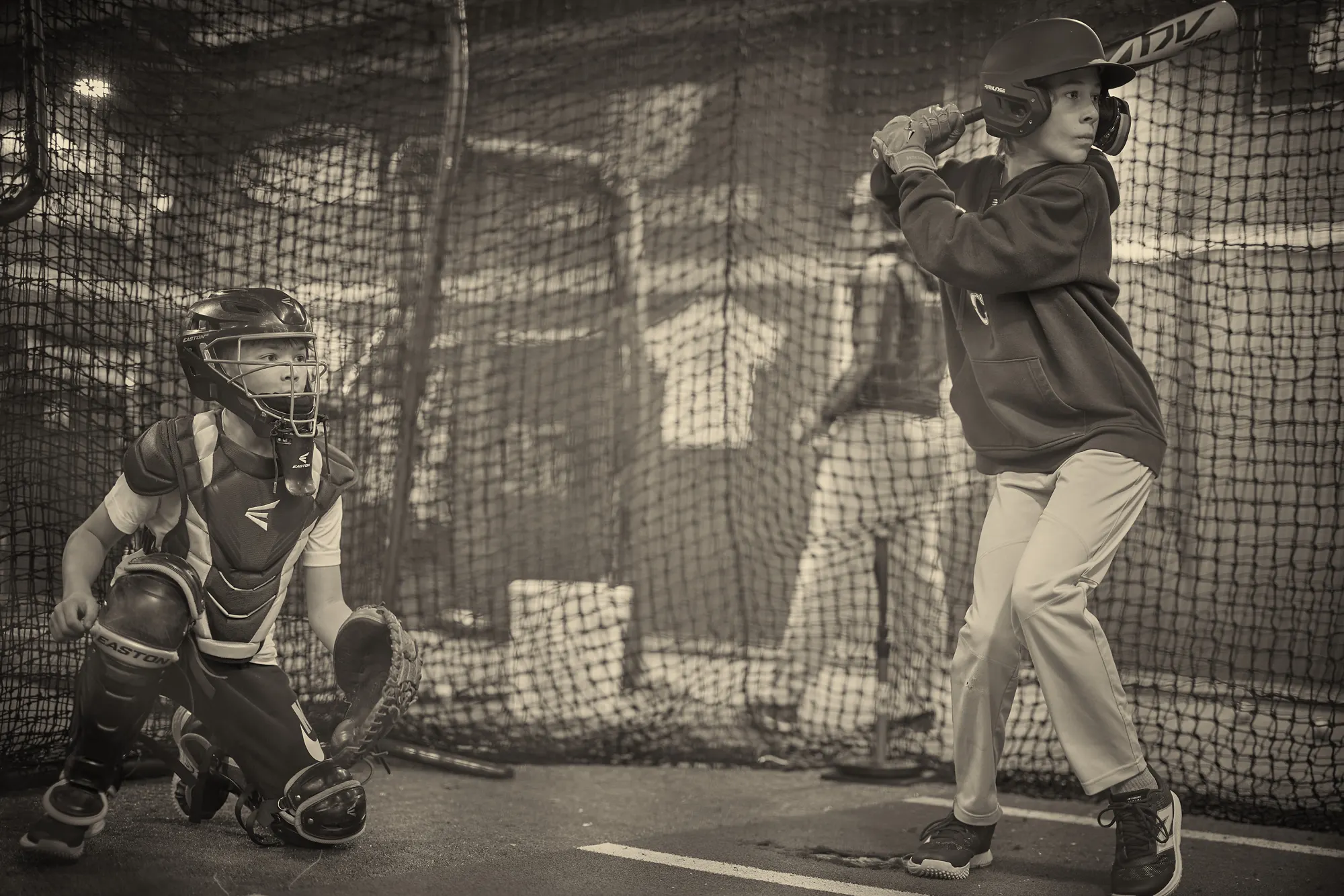 A young hitter in his stance with a catcher behind the plate inside a netted batting cage at Seattle Baseball Academy