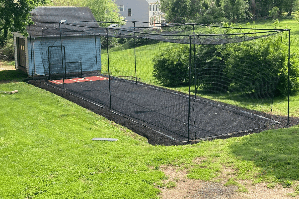 Homeowner-scale batting cage frame by a shed