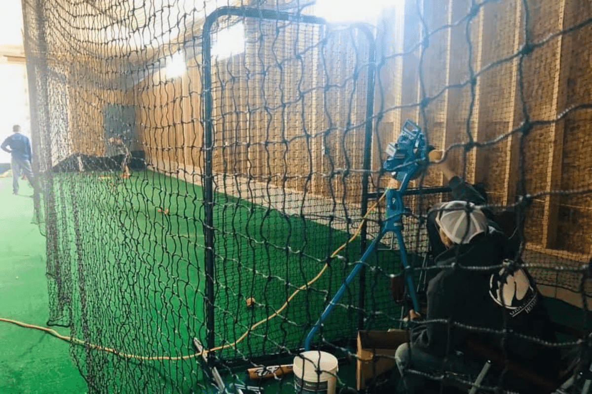 A pitching machine loaded with balls feeding a hitter in an indoor cage