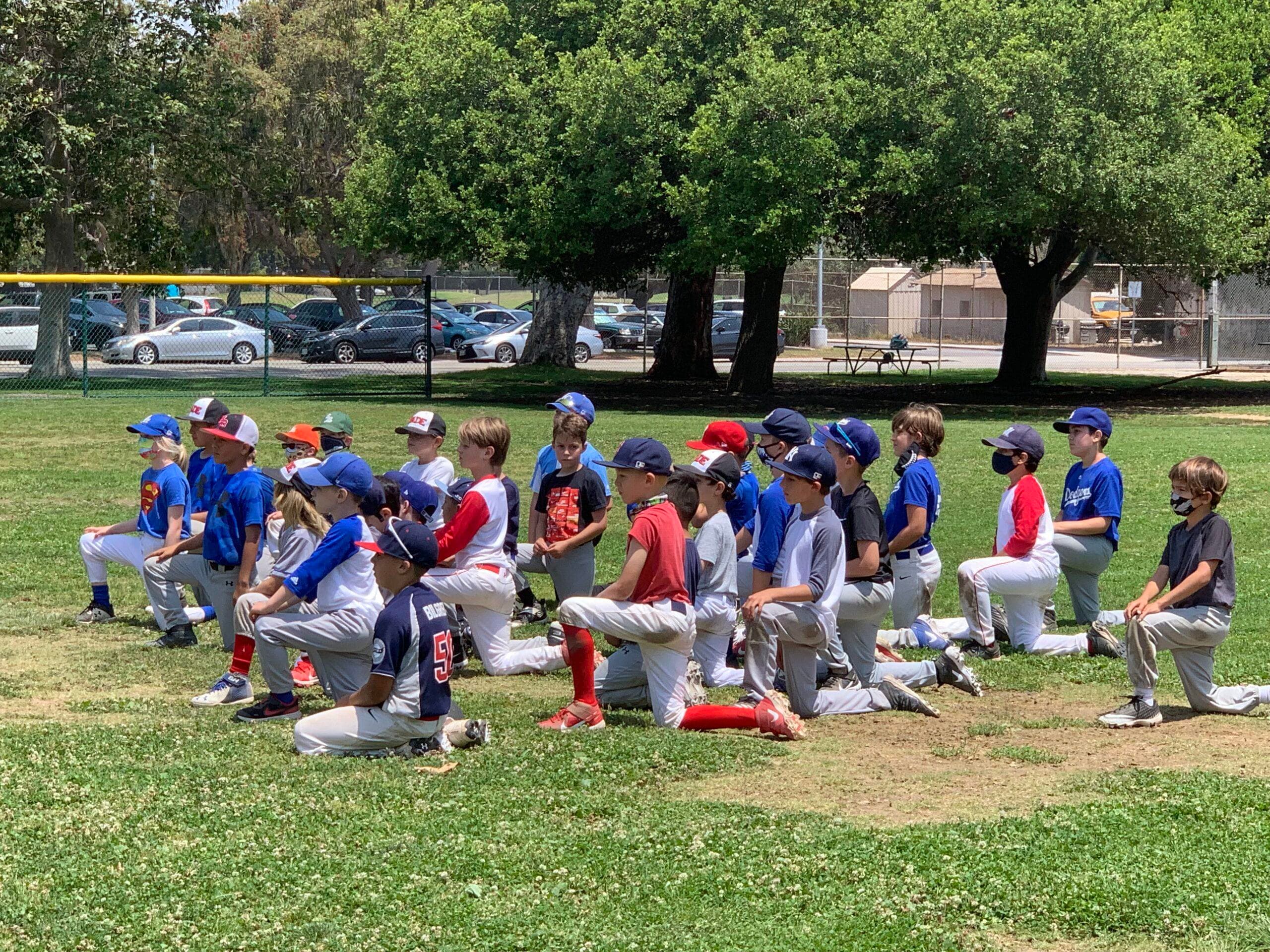 Youth baseball camp players kneeling on a sunny field