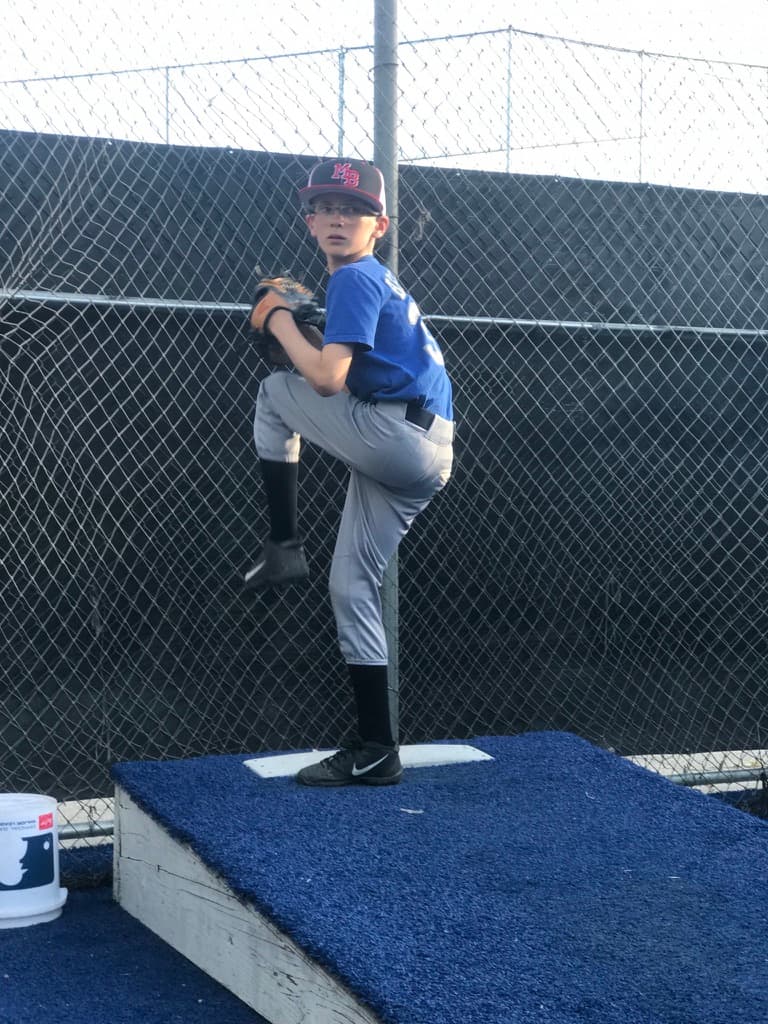 Young batter in sunglasses loading his swing on a dirt infield