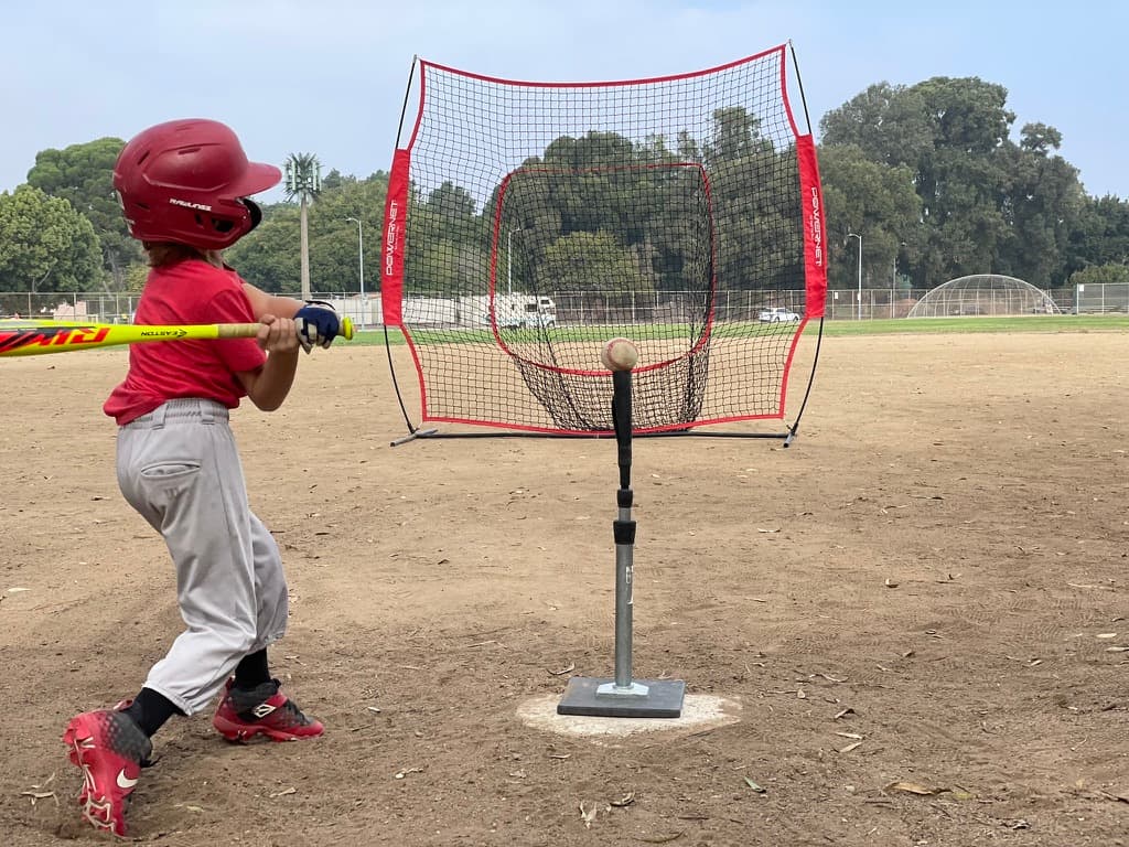 Young hitter practicing off a batting tee into a PowerNet